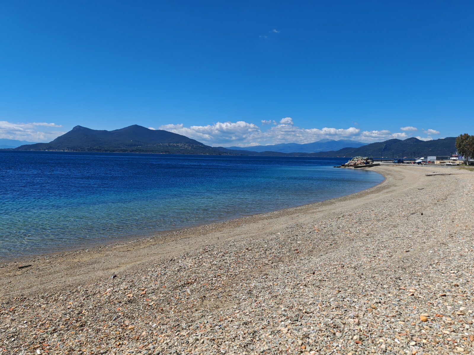 Šljunkovita plaža u luku kod trajektne luke Agiokampos na severnoj Eviji, trajekt uz obalu i planine preko Severnoevojskog zaliva